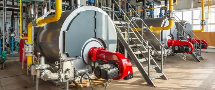 The interior of an industrial boiler room with three large boilers, many pipes, valves and sensors