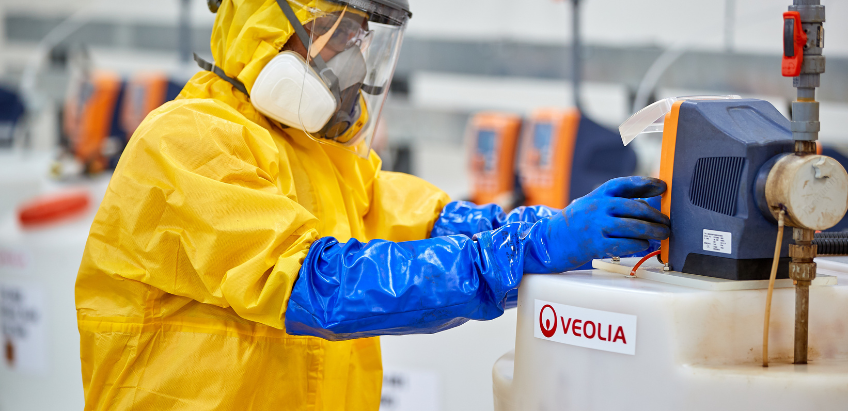 Chemical engineer entering dosing details into a keypad above a chemical container with the Veolia logo attached.